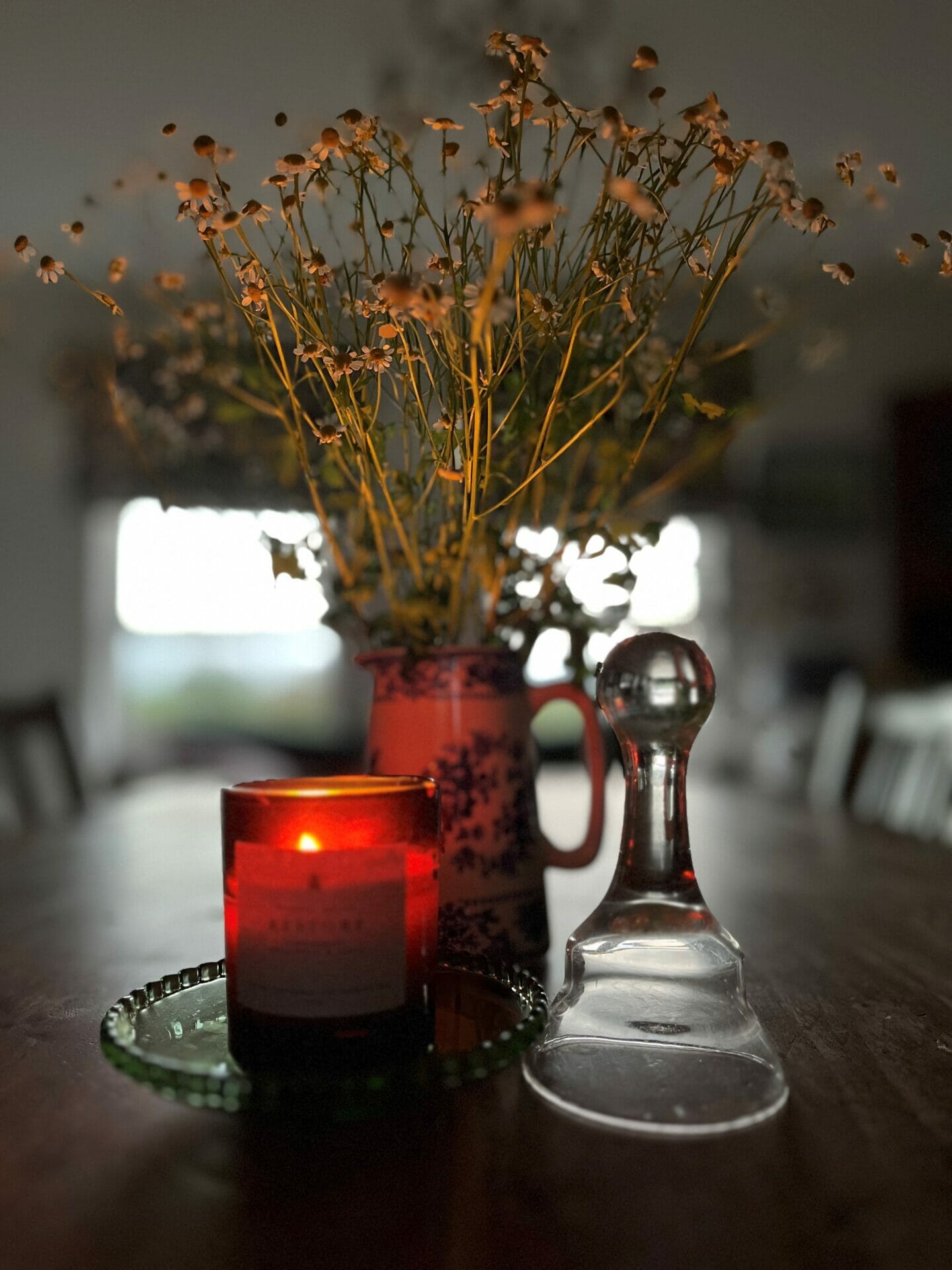 Photograph of lit candle in amber glass beside flowers and candle snuffer