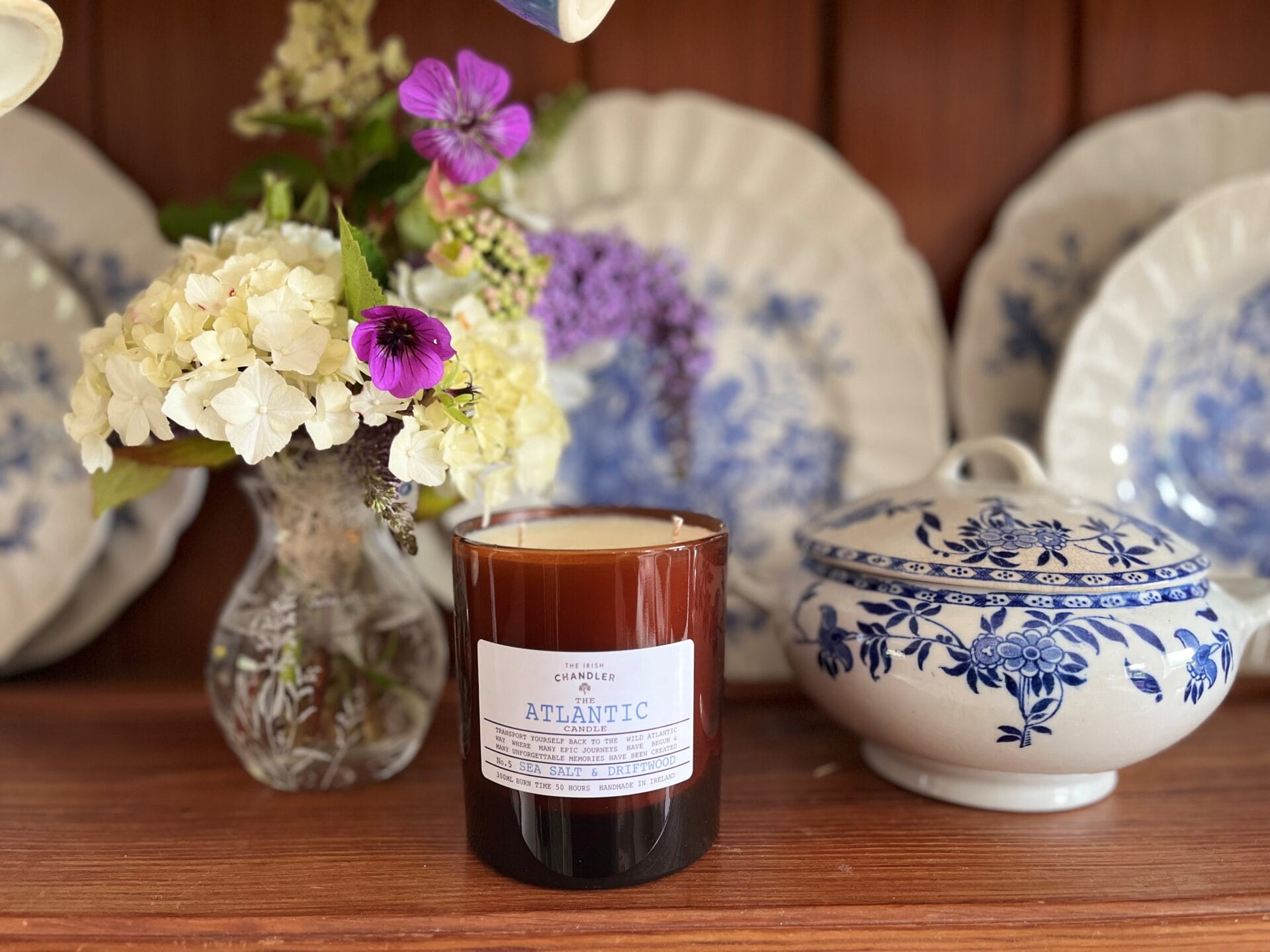 Amber glass candle, called the Atlantic sitting on a shelf beside blue delph.